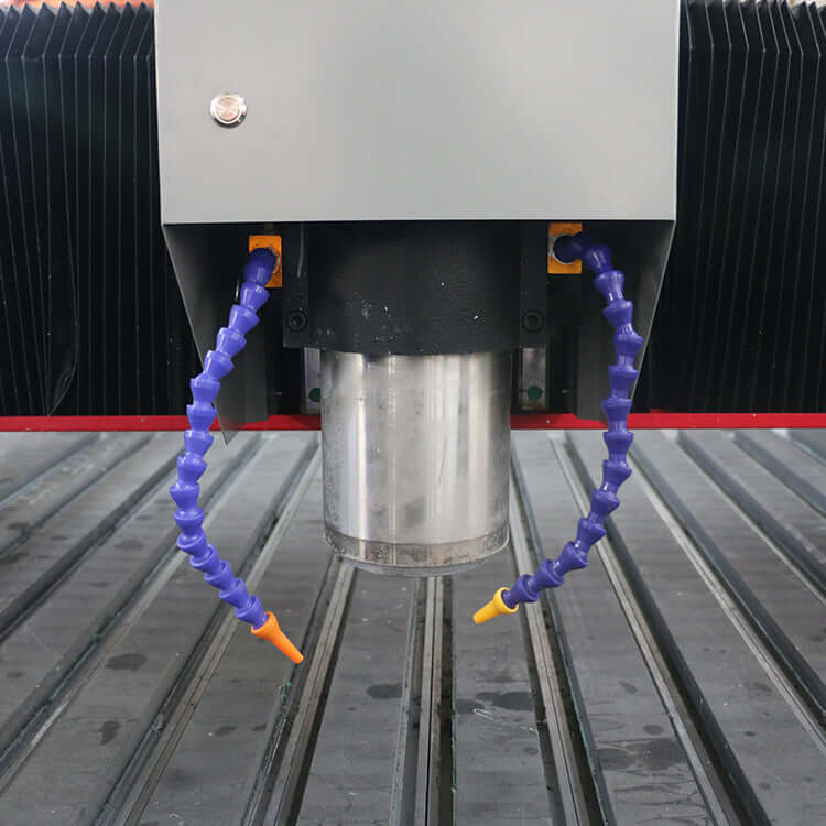 Close-up of a customized metal CNC router spindle with flexible coolant hoses and a grooved work surface.