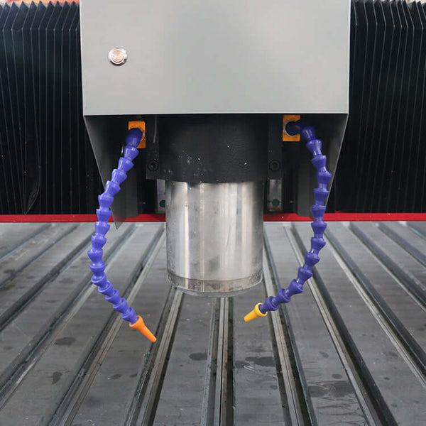 Close-up of a customized metal CNC router spindle with flexible coolant hoses and a grooved work surface.