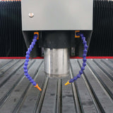 Close-up of a customized metal CNC router spindle with flexible coolant hoses and a grooved work surface.