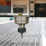 Close-up of a CNC machine spindle over a grid surface, used for precise cutting and engraving in industrial manufacturing.