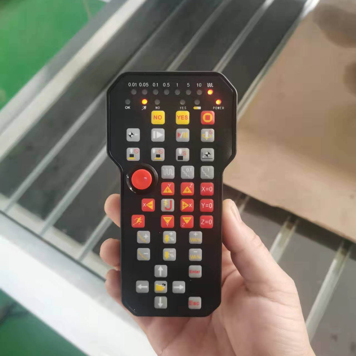 Hand holding a black control handle with multiple buttons on an industrial background, used for machinery operation.