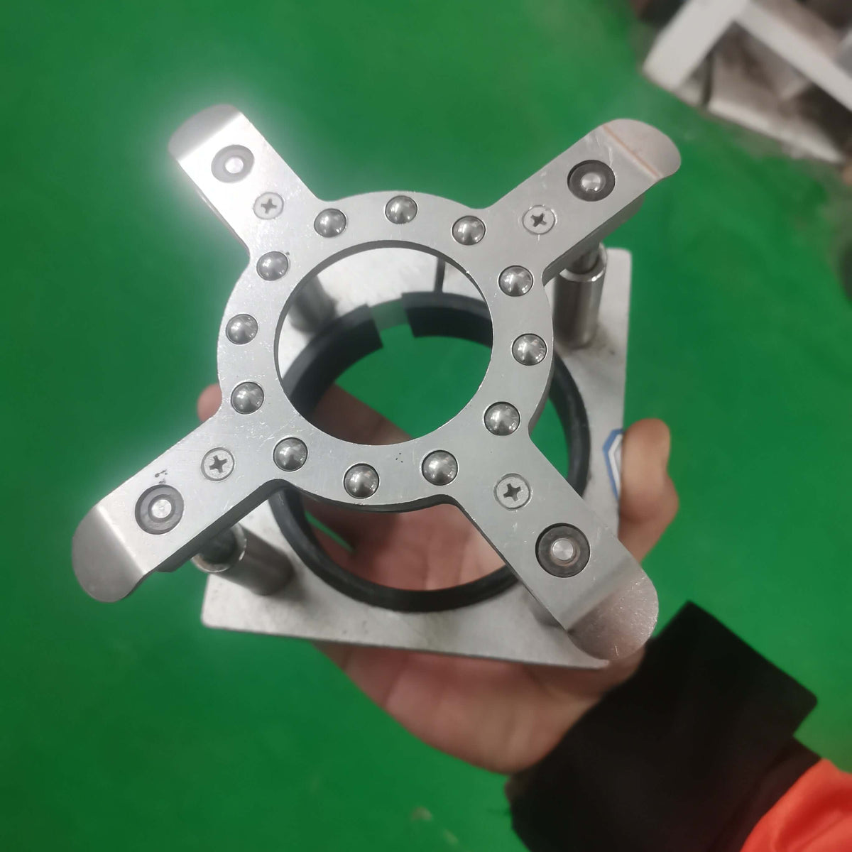 Close-up of a hand holding a silver metal platen press component with screws against a green background.