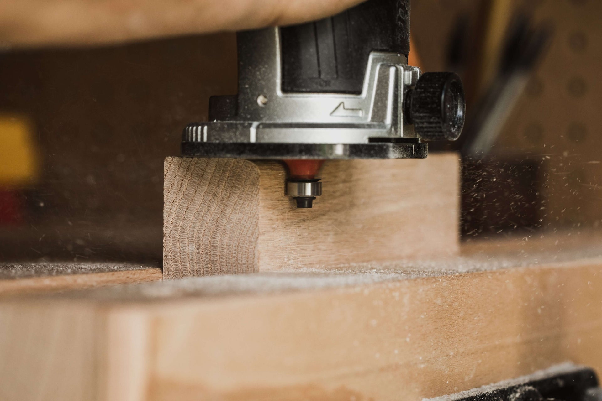 Close-up of a wood router carving a piece of wood in a workshop, with sawdust in the air.